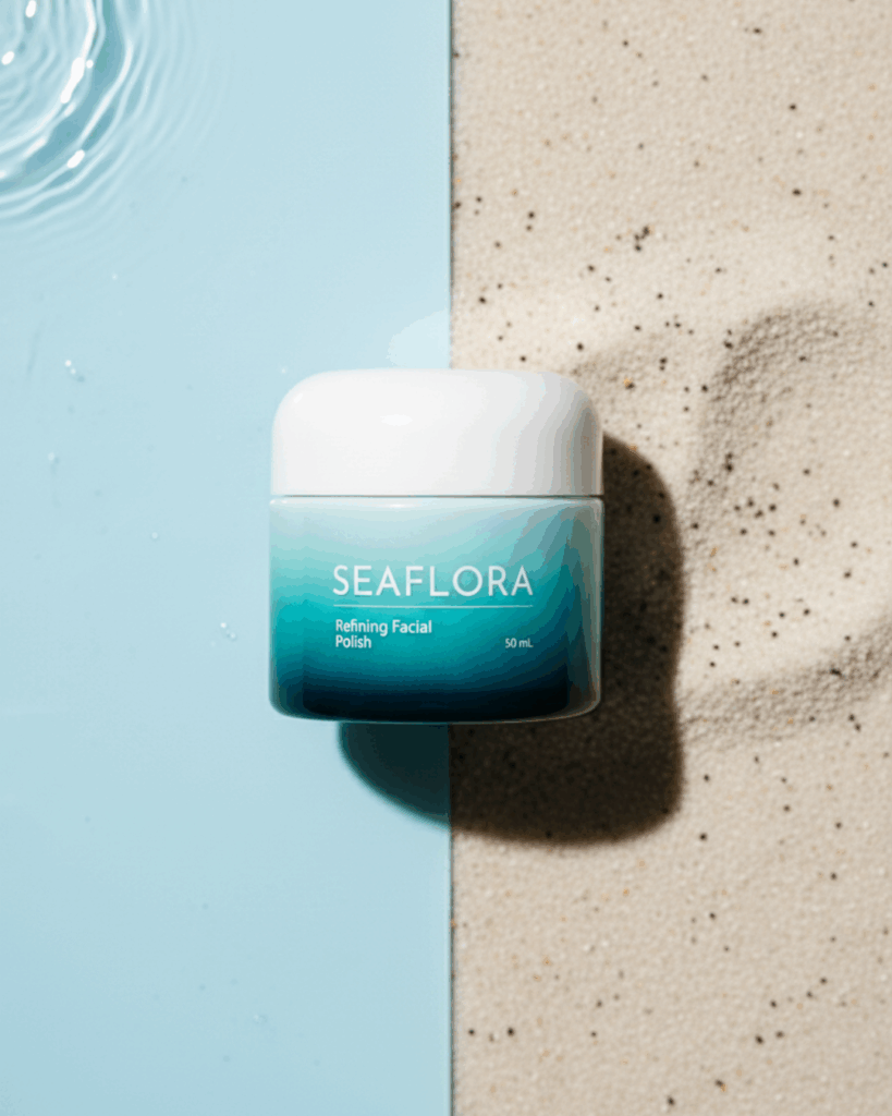 Seaflora-Refining-Facial-Polish-Algae-Exfoliant - Seaflora Skincare Seaflora Refining Facial Polish jar next to a small pile of fine natural exfoliating grains on a surface transitioning to smooth, clear water.